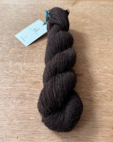 Dark brown skein of wool on a wooden surface with a tag.