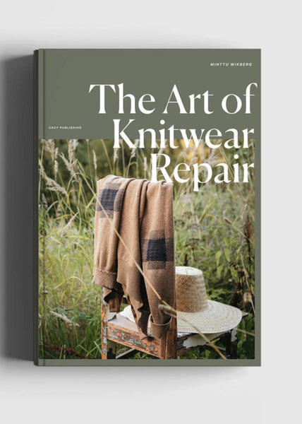 Book titled 'The Art of Knitwear Repair' with a cover featuring a blanket draped over a  chair in a natural outdoor setting.
